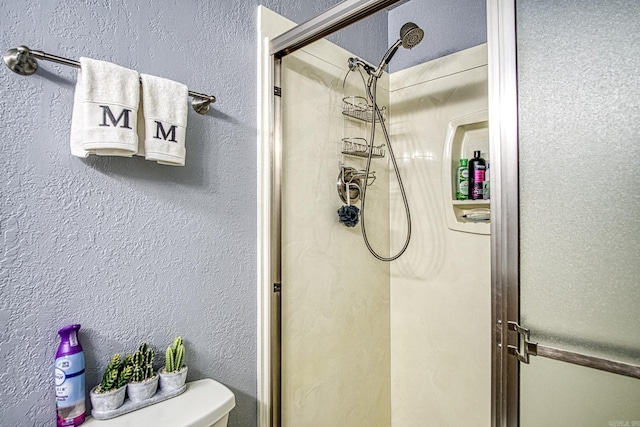 bathroom with toilet, a textured wall, and a stall shower