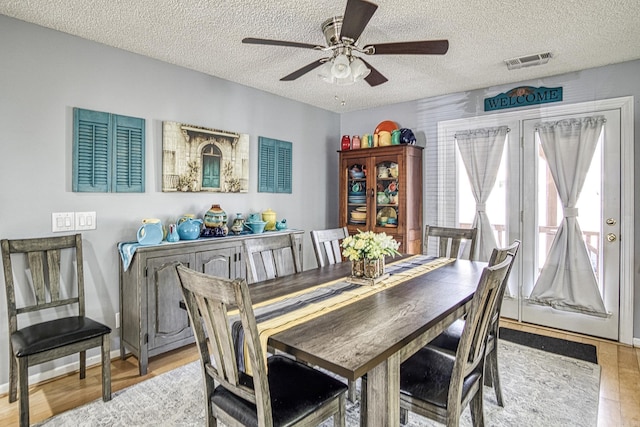 dining room featuring light wood-type flooring, visible vents, and a textured ceiling