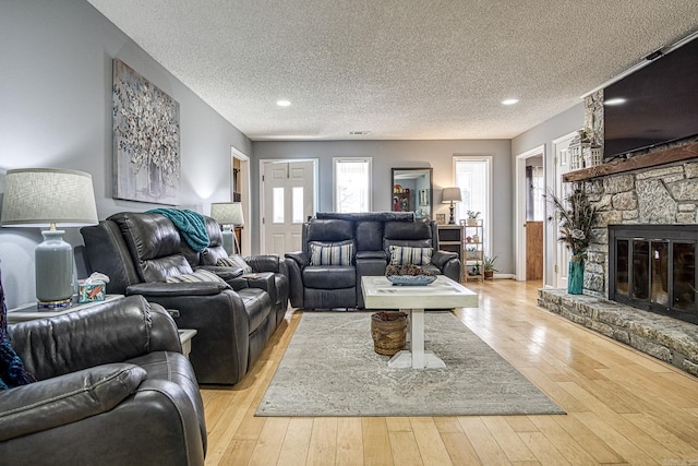 living area featuring a textured ceiling, a stone fireplace, and light wood-style flooring