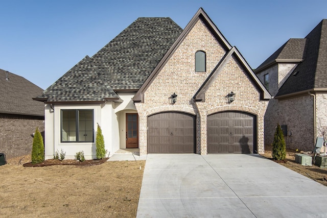 french provincial home with brick siding, an attached garage, concrete driveway, and roof with shingles