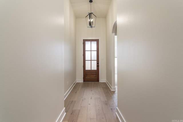 doorway featuring baseboards, light wood-type flooring, a chandelier, and arched walkways