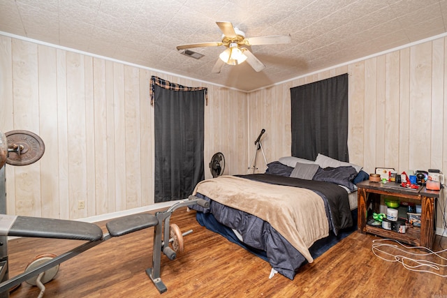 bedroom featuring a ceiling fan, wood finished floors, visible vents, and wood walls