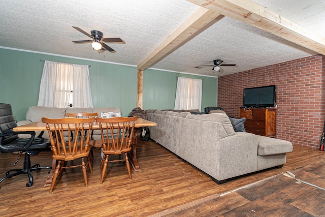 dining space featuring ceiling fan, beamed ceiling, wood finished floors, and brick wall