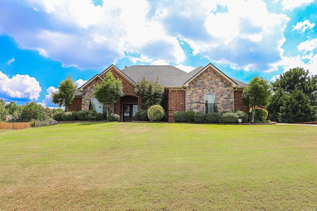 view of front of house featuring brick siding, stone siding, a front yard, and fence