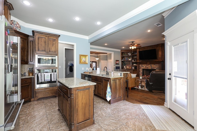 kitchen featuring open floor plan, ornamental molding, a stone fireplace, stainless steel appliances, and a sink