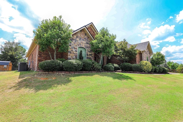 view of front of house featuring brick siding, stone siding, a front yard, and central AC