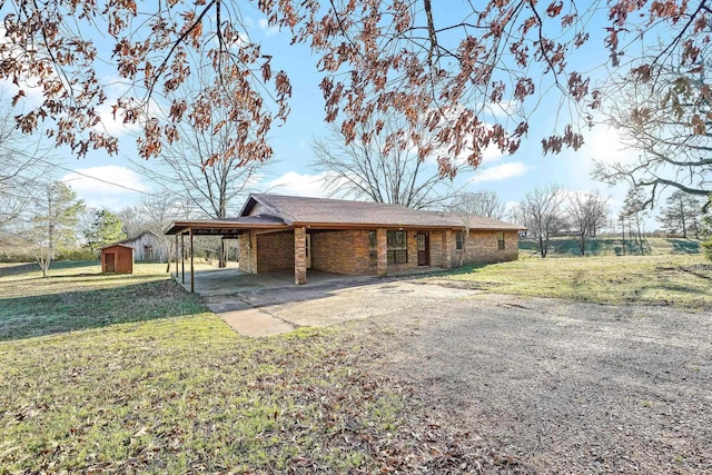 exterior space featuring driveway, an outdoor structure, a front yard, a carport, and brick siding