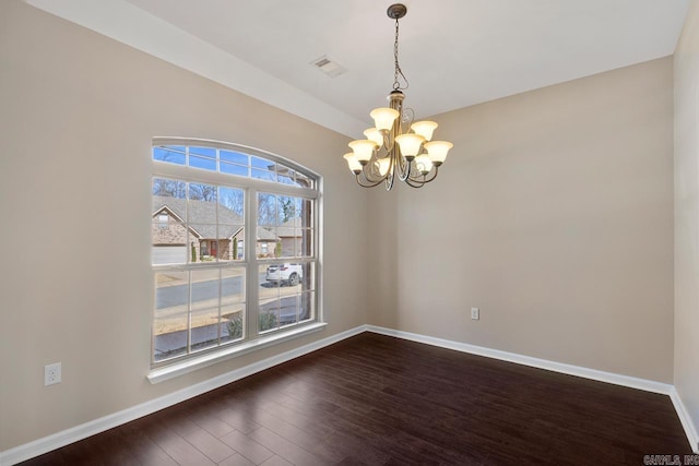 spare room with an inviting chandelier, dark wood-type flooring, visible vents, and baseboards