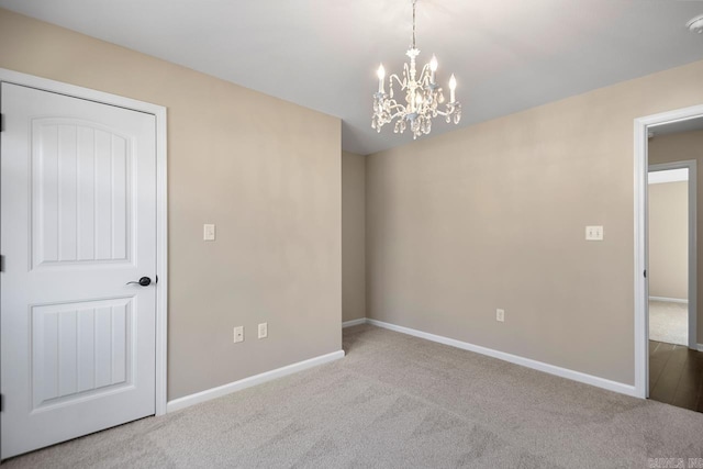 carpeted spare room with a chandelier and baseboards