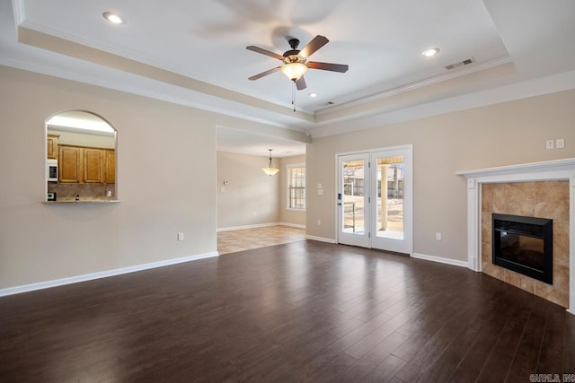 unfurnished living room with wood finished floors, baseboards, visible vents, a tile fireplace, and a raised ceiling