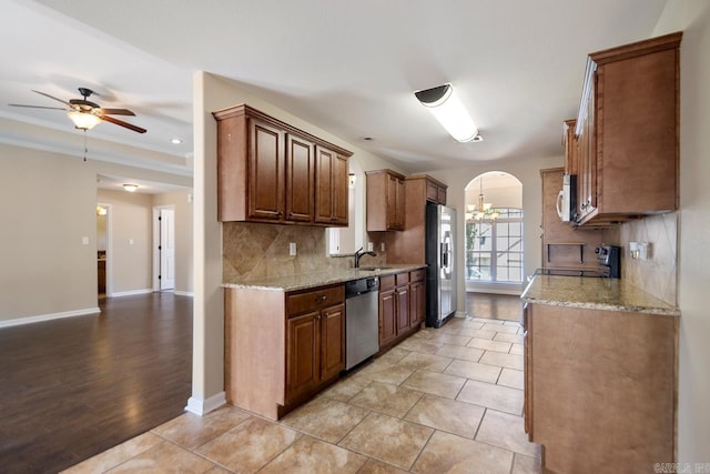 kitchen with arched walkways, a sink, appliances with stainless steel finishes, ceiling fan with notable chandelier, and tasteful backsplash