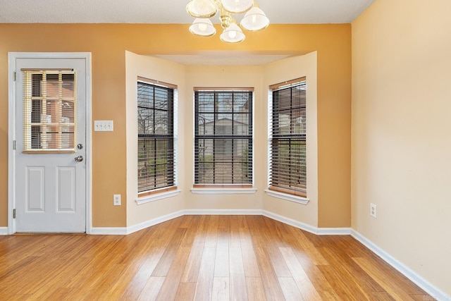 unfurnished dining area with light wood-type flooring, baseboards, and a chandelier