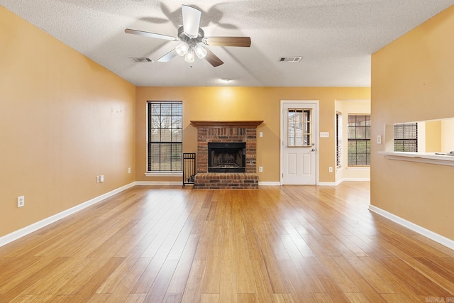 unfurnished living room with visible vents, ceiling fan, a fireplace, and light wood-style floors