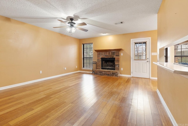 unfurnished living room featuring visible vents, light wood finished floors, ceiling fan, a textured ceiling, and a brick fireplace