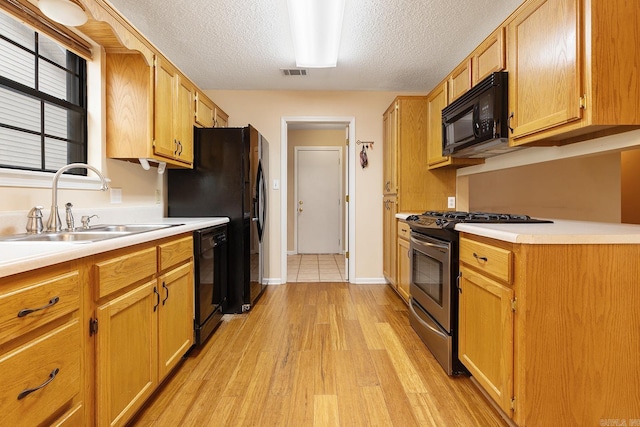 kitchen featuring visible vents, a sink, black appliances, light countertops, and light wood-style floors