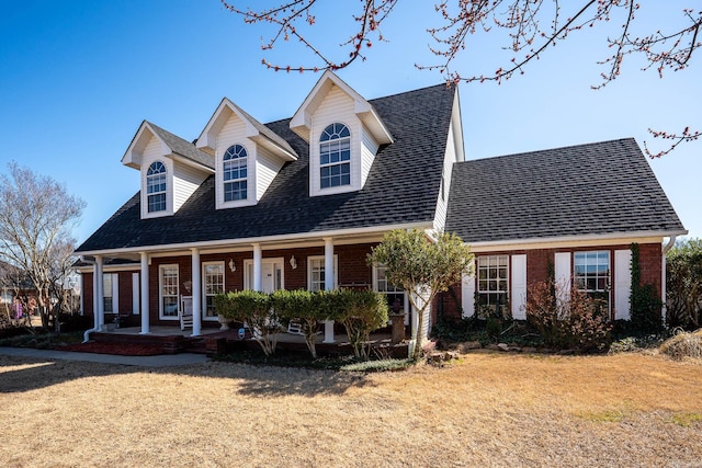 cape cod-style house featuring brick siding, a porch, a front yard, and a shingled roof