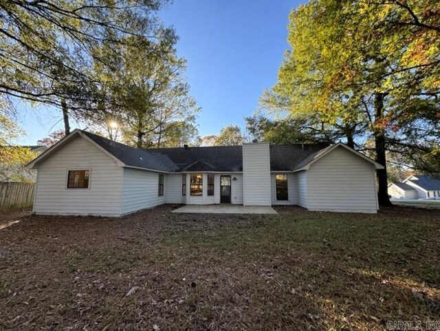 rear view of house with fence, a lawn, a chimney, and a patio area