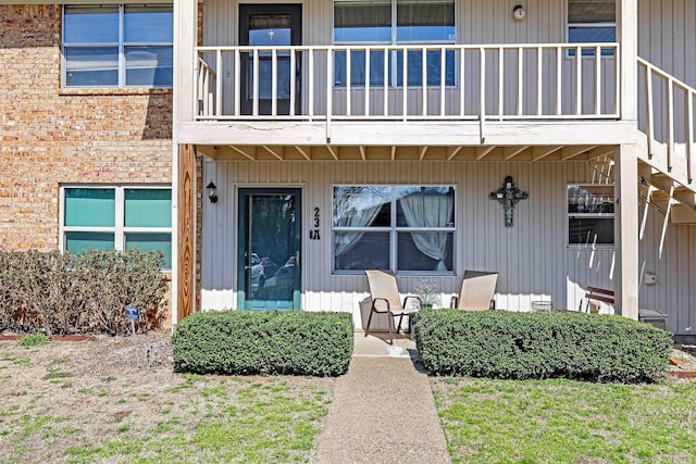 property entrance with a balcony, covered porch, and brick siding