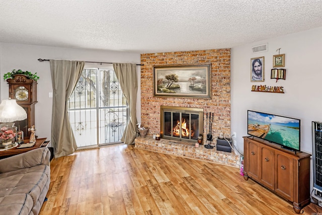 living room with light wood-type flooring, visible vents, a textured ceiling, and a fireplace