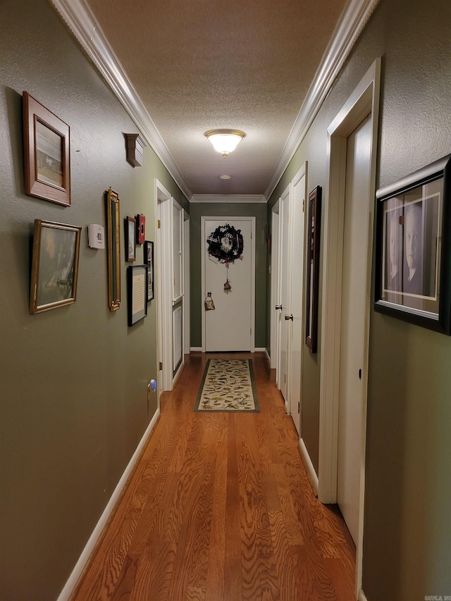 corridor featuring a textured ceiling, crown molding, baseboards, and wood finished floors