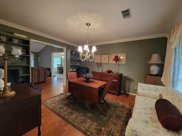 dining area featuring visible vents, baseboards, ornamental molding, wood finished floors, and a notable chandelier