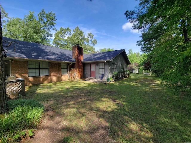 back of property featuring brick siding, a lawn, and a chimney