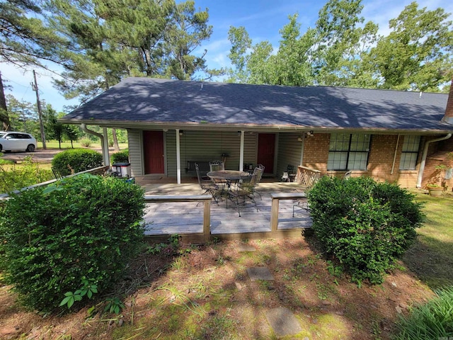 back of house featuring brick siding, a deck, and roof with shingles