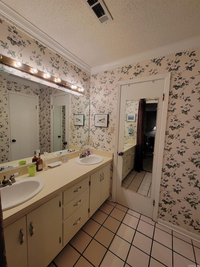 bathroom featuring visible vents, a textured ceiling, wallpapered walls, and a sink