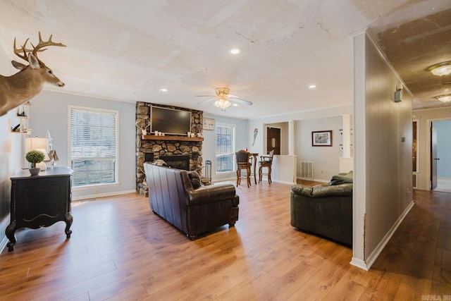 living room featuring visible vents, a stone fireplace, and light wood-style flooring