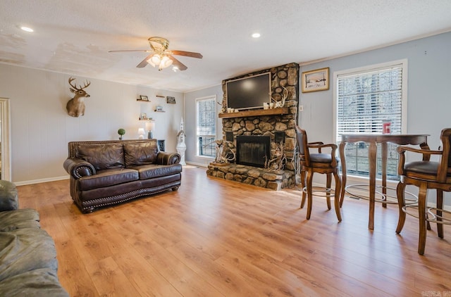 living area with light wood finished floors, a fireplace, a textured ceiling, and ceiling fan