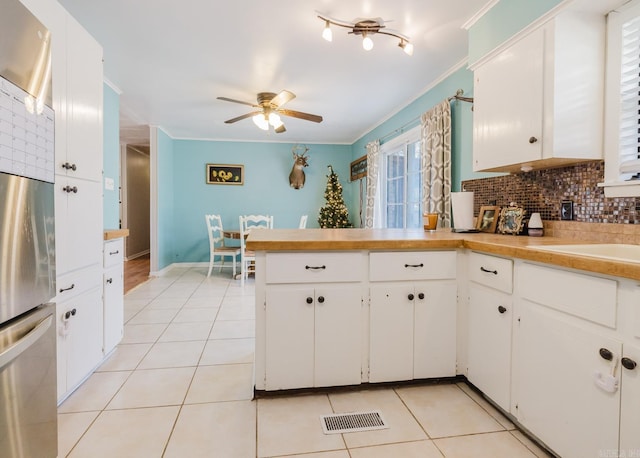 kitchen with a peninsula, light tile patterned flooring, freestanding refrigerator, ornamental molding, and tasteful backsplash