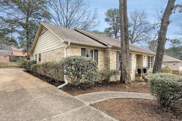 ranch-style home featuring brick siding, a shingled roof, and fence