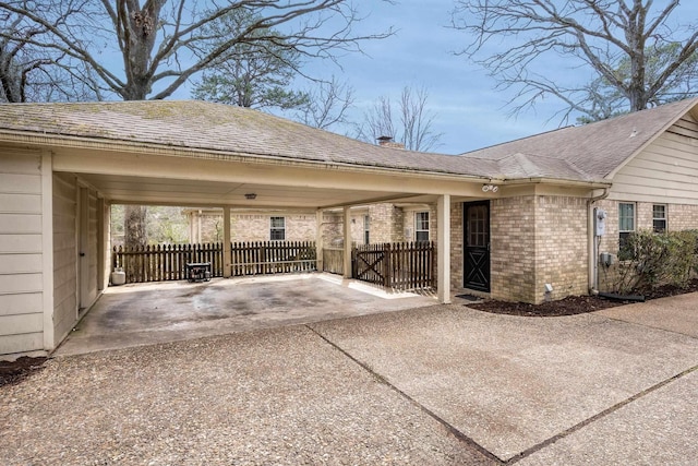 view of side of property with a carport, a shingled roof, brick siding, and fence