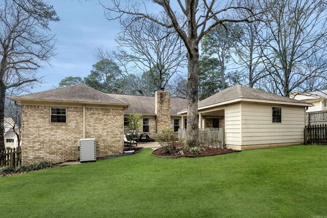 back of house with fence, a yard, a chimney, central air condition unit, and brick siding