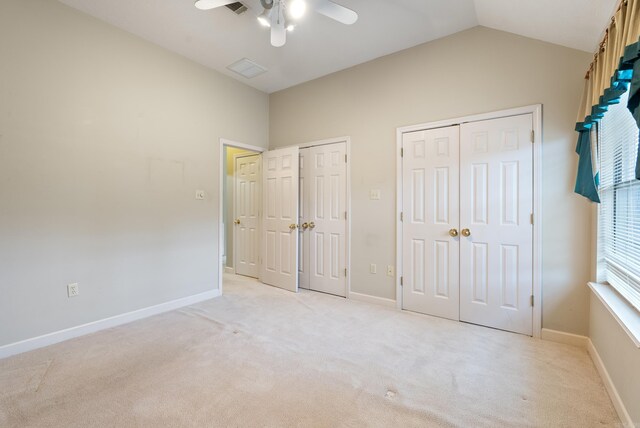 unfurnished bedroom featuring vaulted ceiling, light colored carpet, multiple closets, and baseboards