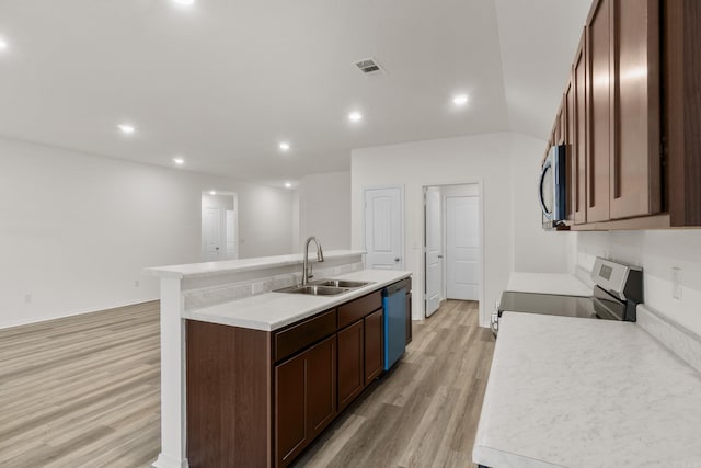 kitchen with a sink, appliances with stainless steel finishes, light wood-style flooring, a center island with sink, and light countertops