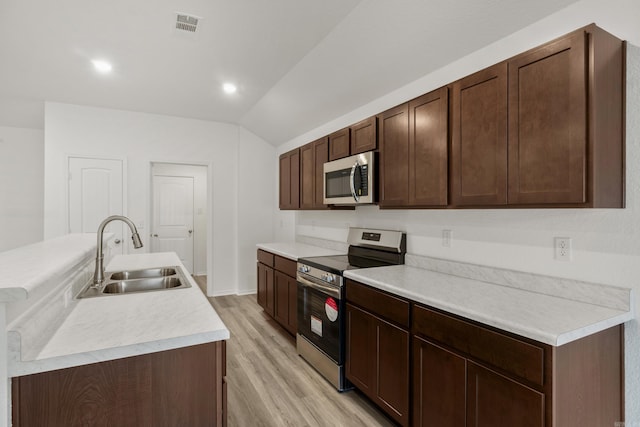 kitchen featuring stainless steel appliances, a sink, light wood-style floors, lofted ceiling, and light countertops