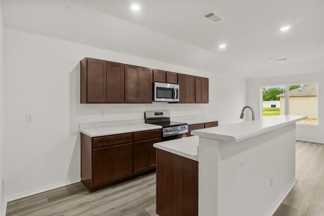 kitchen with appliances with stainless steel finishes, light wood-style flooring, light countertops, recessed lighting, and a center island with sink