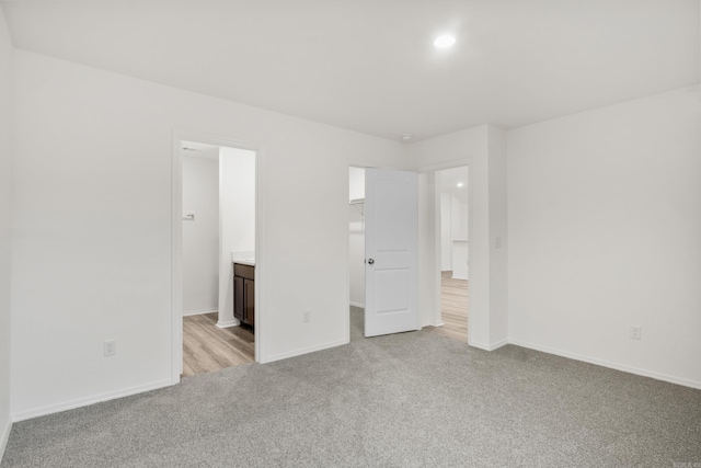 unfurnished bedroom featuring light carpet, a spacious closet, baseboards, connected bathroom, and recessed lighting