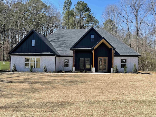 modern farmhouse style home featuring french doors, board and batten siding, roof with shingles, a front yard, and brick siding