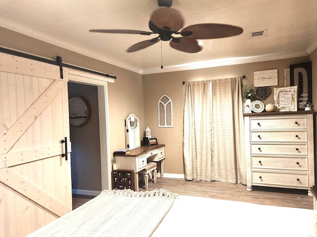 bedroom with a barn door, wood finished floors, crown molding, and visible vents