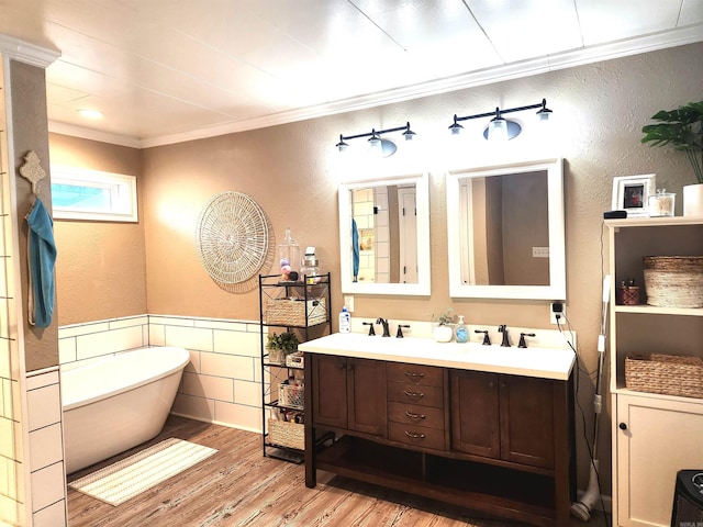 bathroom with wood finished floors, a soaking tub, double vanity, wainscoting, and crown molding