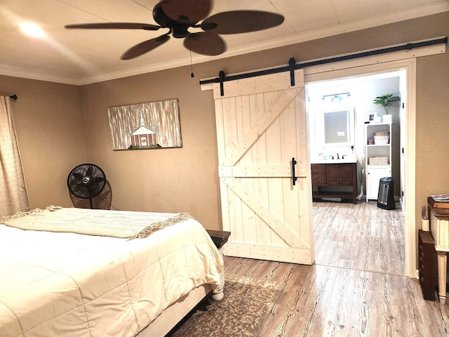 bedroom featuring connected bathroom, ceiling fan, a barn door, ornamental molding, and wood finished floors