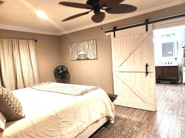 bedroom with wood finished floors, a sink, ceiling fan, ornamental molding, and a barn door