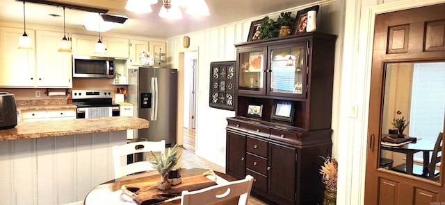 kitchen featuring an inviting chandelier, a peninsula, stainless steel appliances, light countertops, and pendant lighting