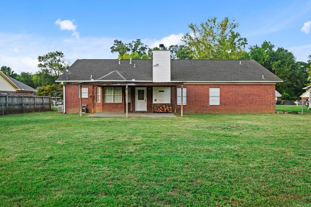 rear view of property featuring a patio, fence, a yard, a chimney, and brick siding