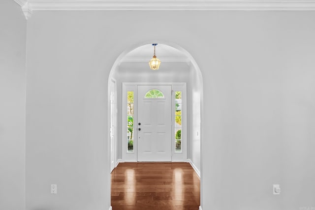 foyer featuring baseboards, wood finished floors, arched walkways, and ornamental molding