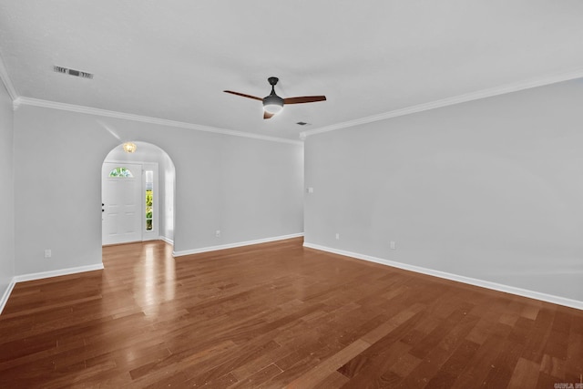 empty room featuring arched walkways, ornamental molding, baseboards, and wood finished floors