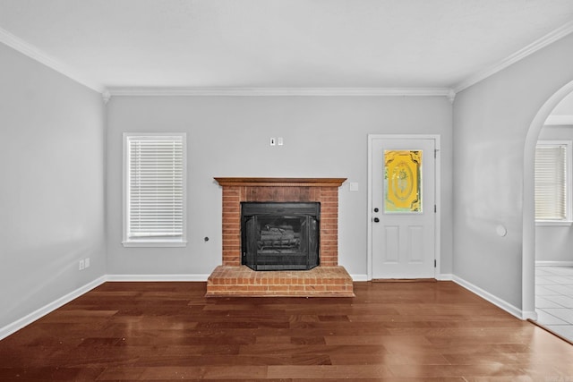 unfurnished living room with baseboards, ornamental molding, a fireplace, wood finished floors, and arched walkways