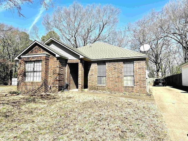 view of front of house featuring brick siding, roof with shingles, and fence